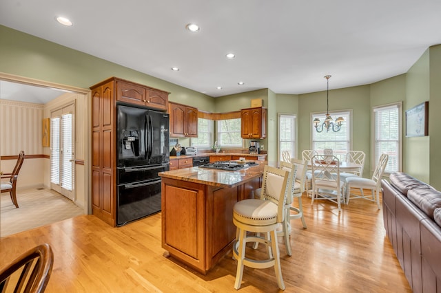 kitchen with light wood-type flooring, black refrigerator with ice dispenser, a center island, decorative light fixtures, and light stone counters