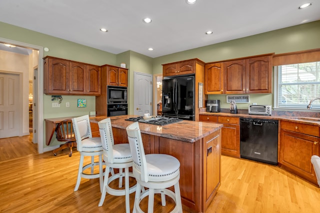 kitchen with a kitchen island, a breakfast bar, black appliances, light hardwood / wood-style floors, and sink