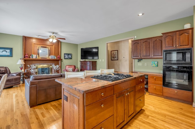 kitchen with ceiling fan, light hardwood / wood-style flooring, black appliances, a fireplace, and a center island