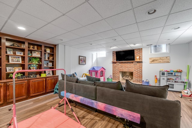 living room with light hardwood / wood-style flooring, a paneled ceiling, and a brick fireplace