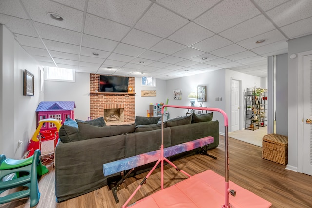 living room featuring a drop ceiling, a brick fireplace, and hardwood / wood-style flooring