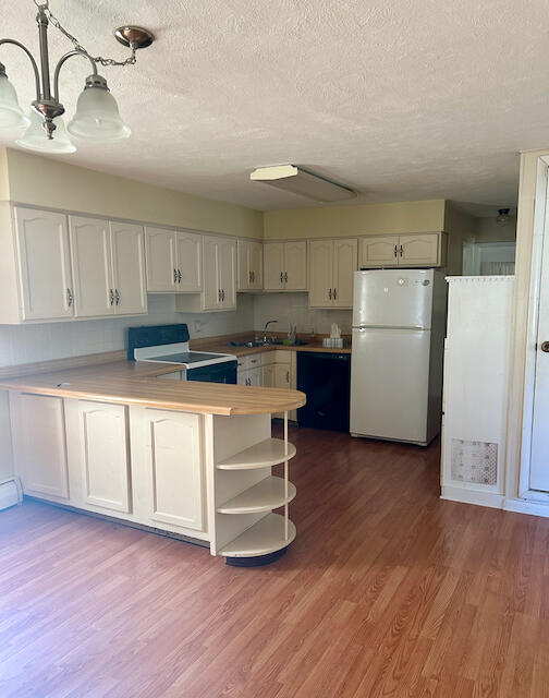 kitchen with black appliances, wood-type flooring, kitchen peninsula, white cabinetry, and pendant lighting