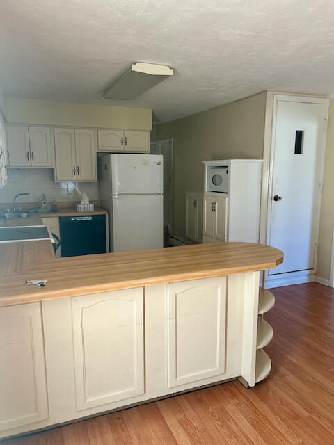 kitchen with white appliances, light hardwood / wood-style floors, kitchen peninsula, and backsplash