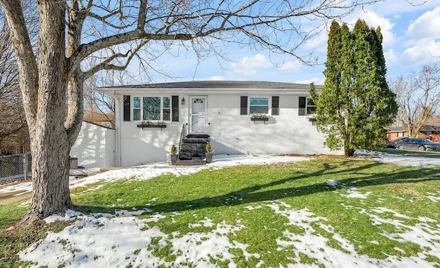 ranch-style house featuring entry steps, brick siding, fence, and a yard