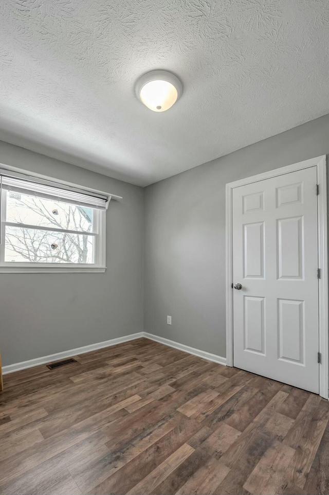 unfurnished room featuring baseboards, a textured ceiling, visible vents, and dark wood-style flooring