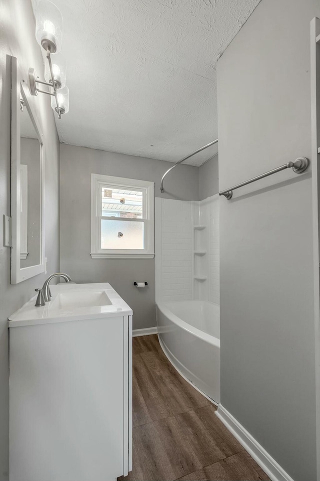 full bathroom with baseboards, wood finished floors,  shower combination, a textured ceiling, and vanity