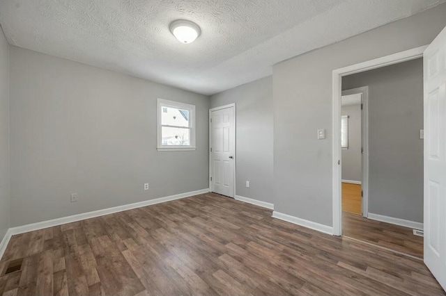 unfurnished bedroom with a textured ceiling, a closet, dark wood finished floors, and baseboards