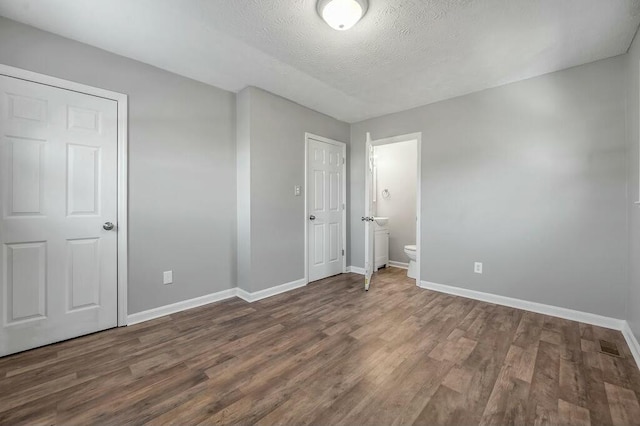 unfurnished bedroom with a textured ceiling, dark wood-style flooring, and baseboards