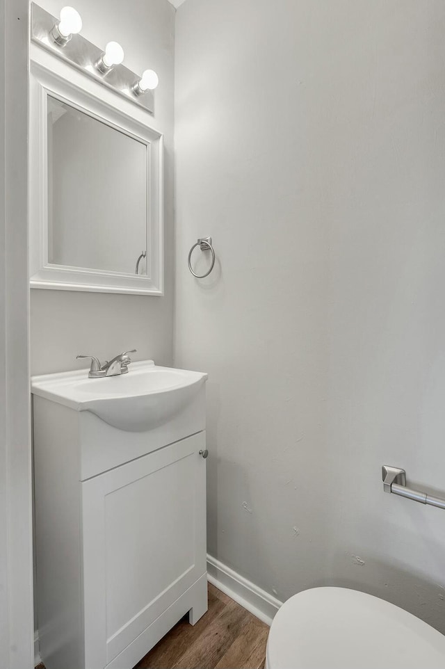 half bath with toilet, baseboards, wood finished floors, and vanity