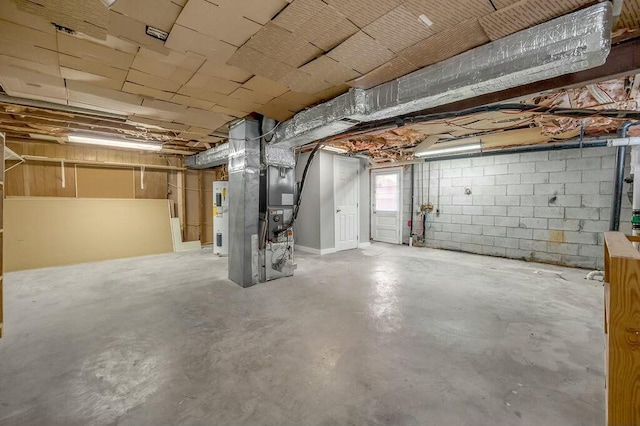 basement featuring concrete block wall, electric water heater, and heating unit