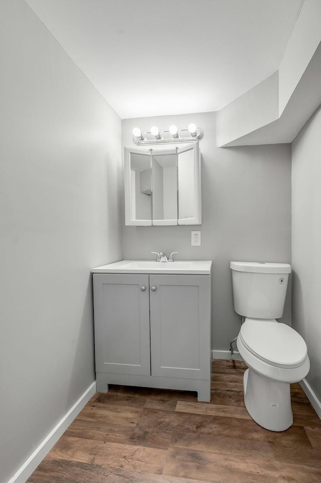 half bath featuring wood finished floors, toilet, and baseboards