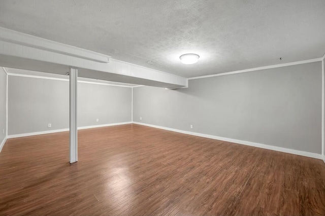 finished basement featuring a textured ceiling, baseboards, dark wood-type flooring, and ornamental molding