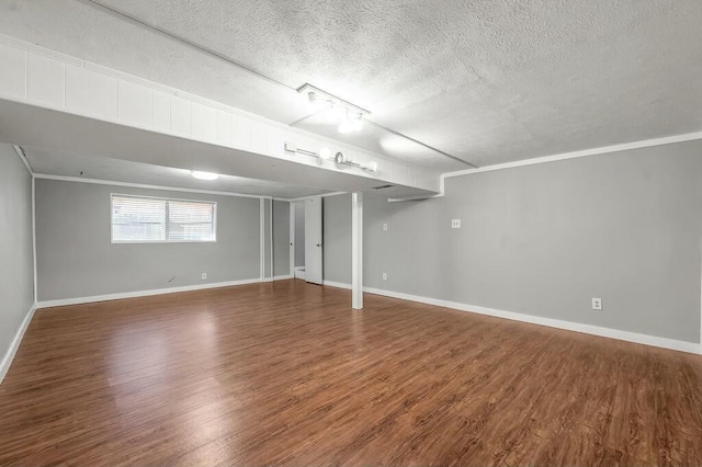 below grade area with a textured ceiling, baseboards, dark wood finished floors, and crown molding