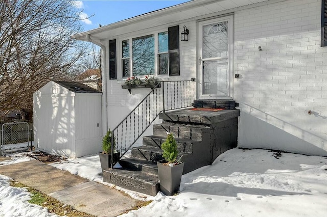 snow covered property entrance featuring brick siding and fence