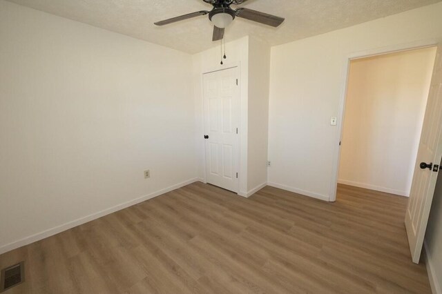 unfurnished bedroom featuring a textured ceiling, wood-type flooring, ceiling fan, and a closet