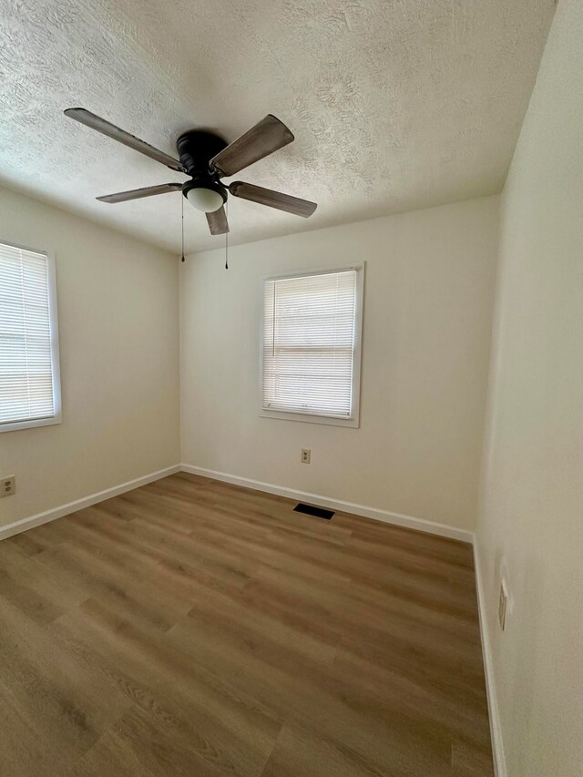 spare room featuring a textured ceiling, a healthy amount of sunlight, and dark hardwood / wood-style floors