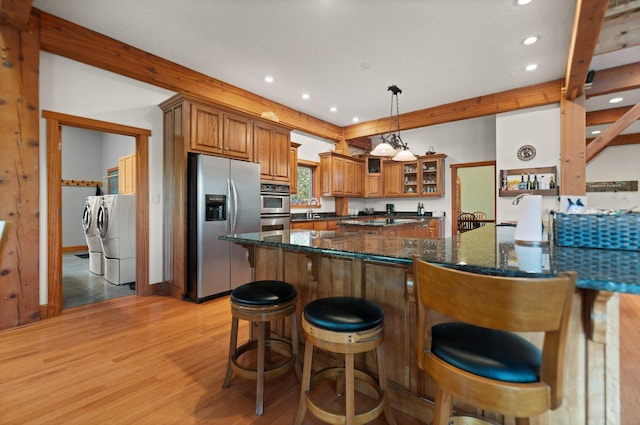 kitchen featuring brown cabinetry, dark stone counters, glass insert cabinets, stainless steel appliances, and pendant lighting