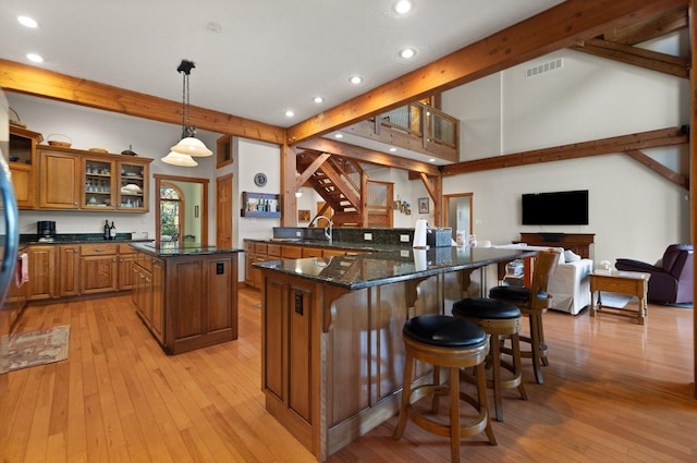 kitchen featuring visible vents, glass insert cabinets, a breakfast bar, open floor plan, and decorative light fixtures