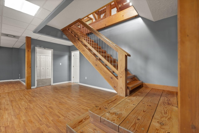 below grade area with a paneled ceiling, wood finished floors, baseboards, and stairs