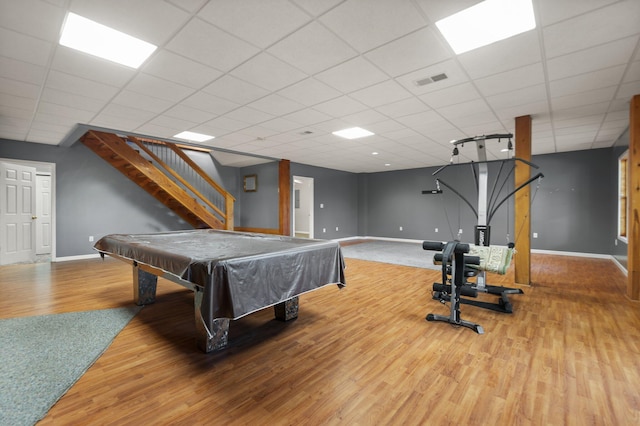 recreation room with a paneled ceiling, visible vents, baseboards, and wood finished floors