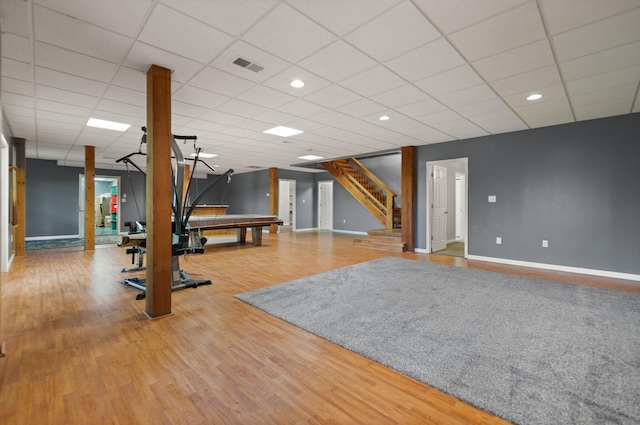 exercise room with a paneled ceiling, visible vents, baseboards, and wood finished floors