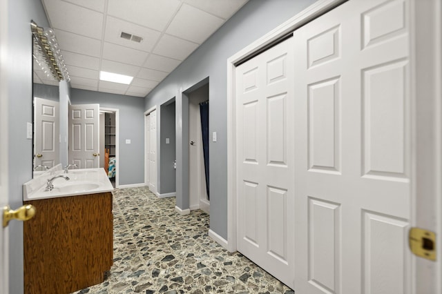 full bath with a paneled ceiling, visible vents, baseboards, and double vanity