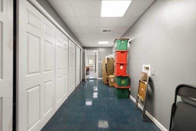 hallway featuring a paneled ceiling, visible vents, baseboards, and concrete flooring