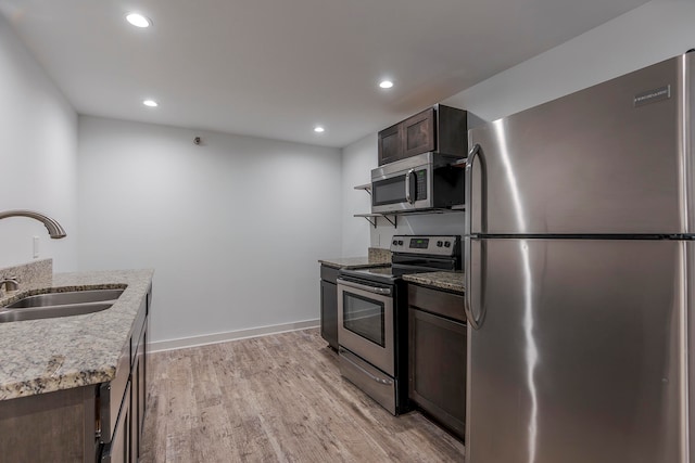 kitchen featuring appliances with stainless steel finishes, dark brown cabinets, light stone countertops, sink, and light hardwood / wood-style floors