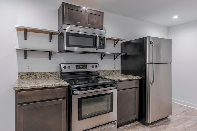 kitchen with stainless steel appliances, light hardwood / wood-style floors, light stone countertops, and dark brown cabinetry