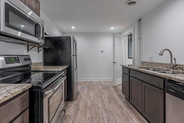 kitchen featuring stainless steel appliances, dark brown cabinetry, sink, light stone counters, and light wood-type flooring