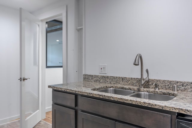 kitchen featuring dark brown cabinetry, sink, light stone counters, and light hardwood / wood-style flooring