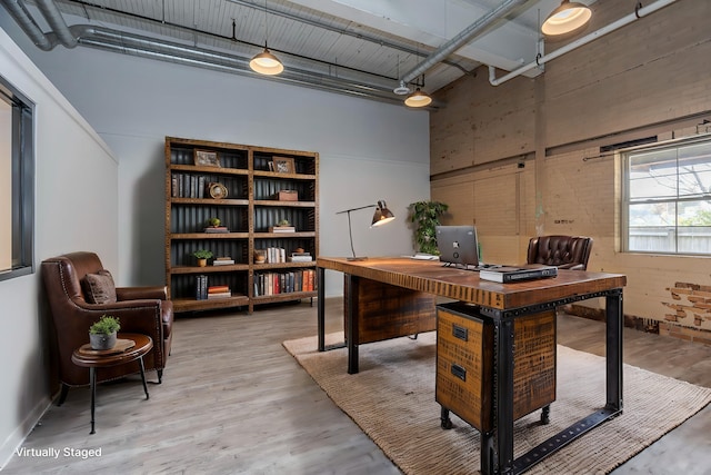 home office with a towering ceiling and light wood-type flooring