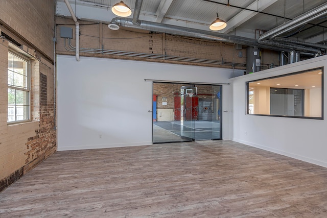 spare room featuring a towering ceiling, brick wall, and hardwood / wood-style flooring