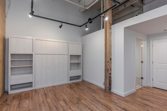 interior space with a towering ceiling, rail lighting, and light hardwood / wood-style flooring