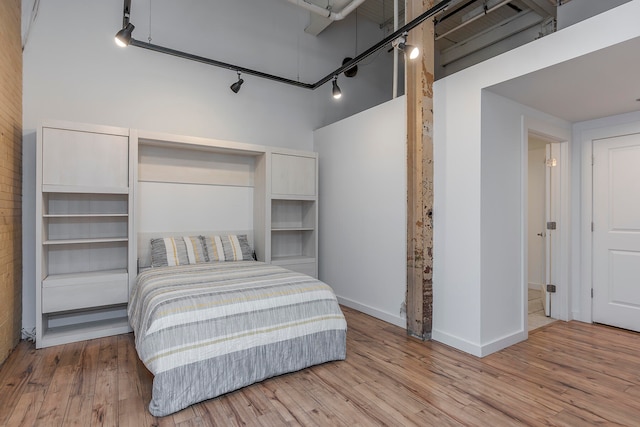 bedroom featuring a towering ceiling, rail lighting, and light wood-type flooring