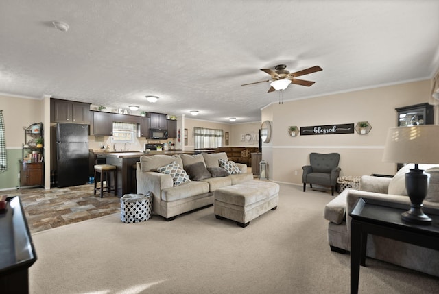 living room featuring ceiling fan, ornamental molding, a textured ceiling, and light colored carpet