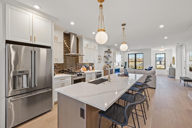 kitchen featuring white cabinetry, sink, wall chimney range hood, an island with sink, and high end appliances