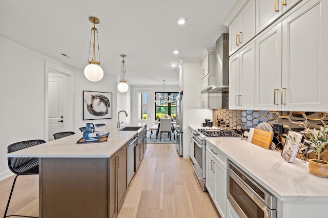 kitchen with stainless steel appliances, wall chimney range hood, a spacious island, decorative light fixtures, and a kitchen bar