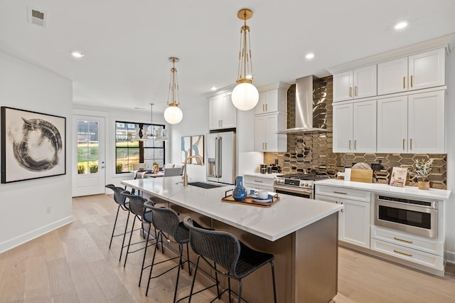 kitchen featuring white cabinetry, a kitchen island with sink, wall chimney exhaust hood, and high end appliances