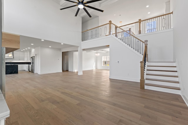 unfurnished living room with ceiling fan, a towering ceiling, and hardwood / wood-style floors