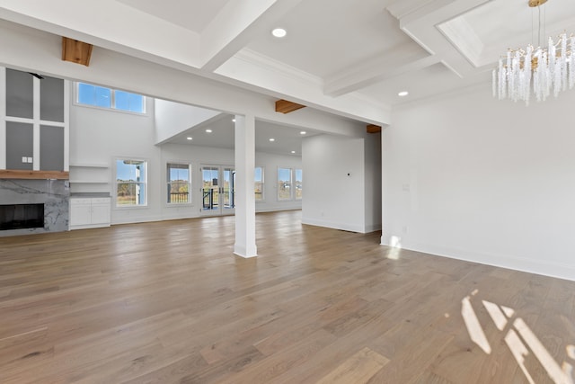 unfurnished living room featuring beam ceiling, hardwood / wood-style floors, a fireplace, and an inviting chandelier