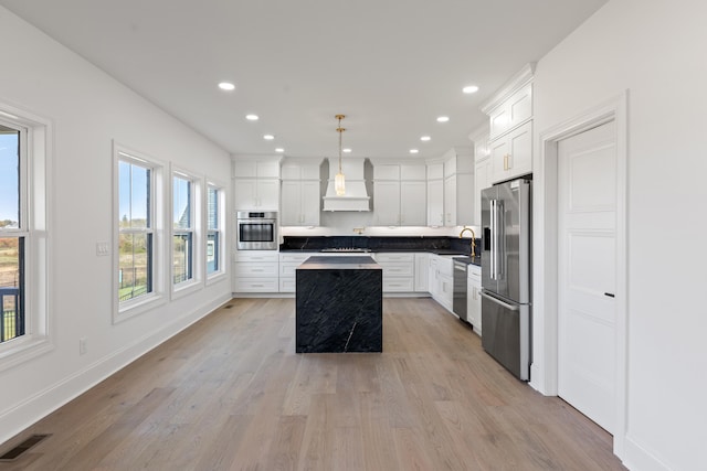 kitchen featuring custom exhaust hood, hanging light fixtures, appliances with stainless steel finishes, light hardwood / wood-style floors, and a center island