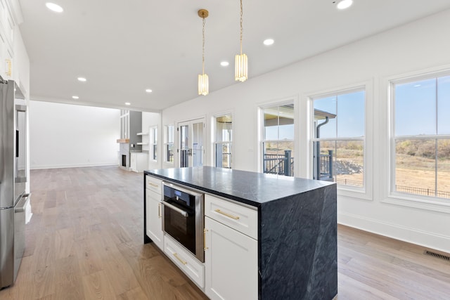 kitchen with a wealth of natural light, white cabinets, stainless steel appliances, and light wood-type flooring