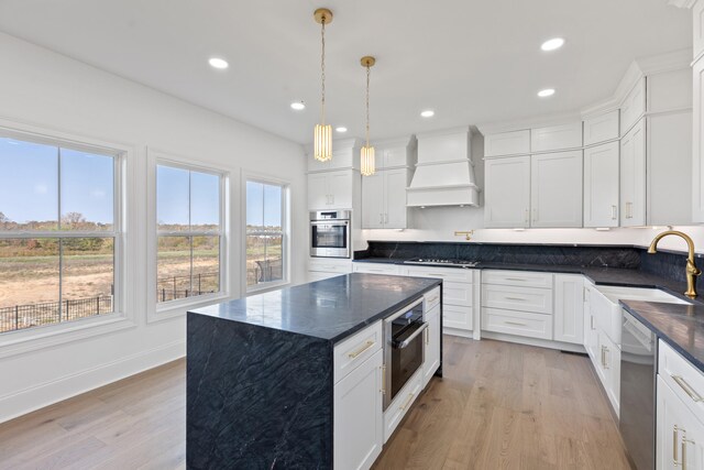 kitchen with a kitchen island, custom exhaust hood, stainless steel appliances, and light hardwood / wood-style floors