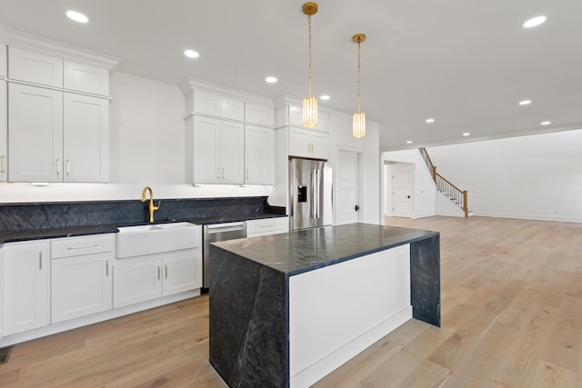 kitchen with hanging light fixtures, appliances with stainless steel finishes, white cabinetry, light hardwood / wood-style floors, and sink