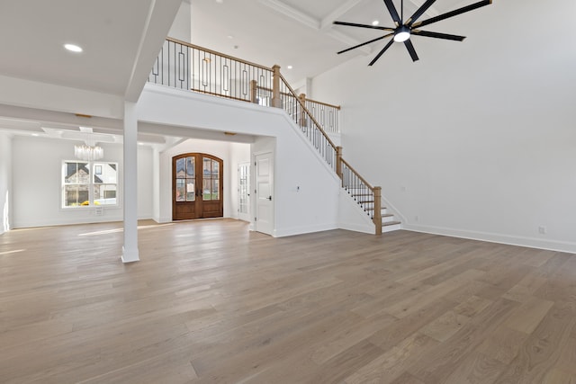 unfurnished living room with french doors, a towering ceiling, ceiling fan with notable chandelier, and hardwood / wood-style floors