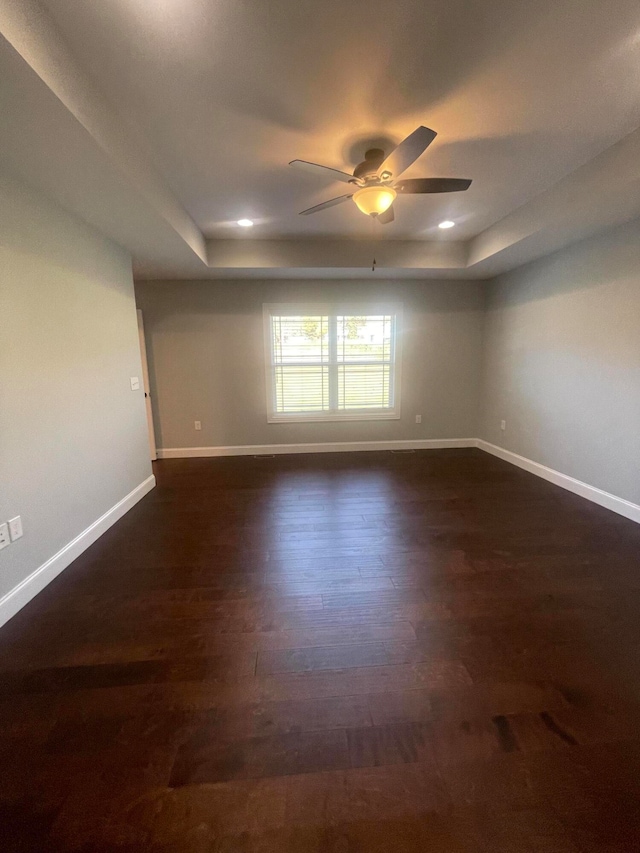 spare room featuring a raised ceiling, ceiling fan, and dark hardwood / wood-style flooring