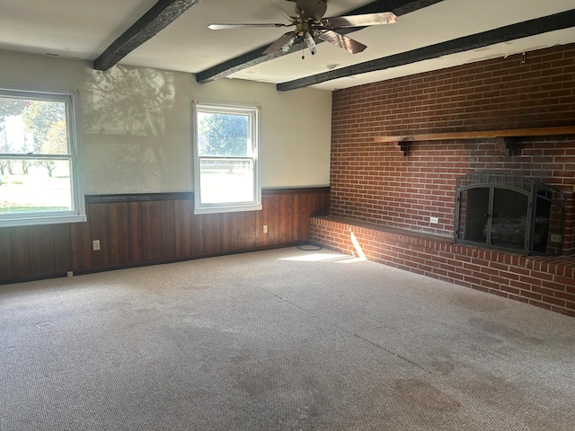 unfurnished living room with carpet floors, beam ceiling, ceiling fan, a fireplace, and wood walls