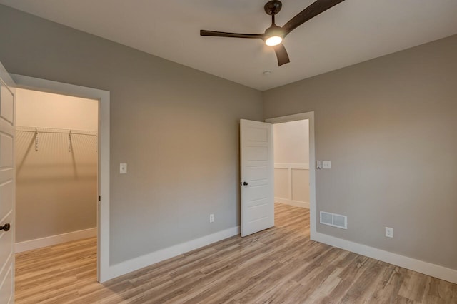 unfurnished bedroom featuring a spacious closet, a closet, light hardwood / wood-style floors, and ceiling fan