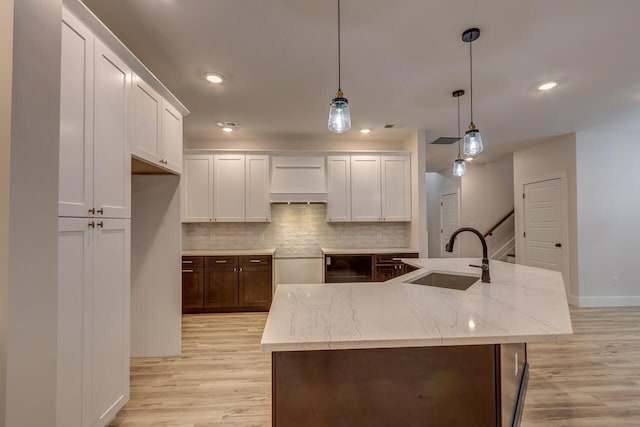 kitchen with light hardwood / wood-style floors, decorative light fixtures, a kitchen island with sink, and sink